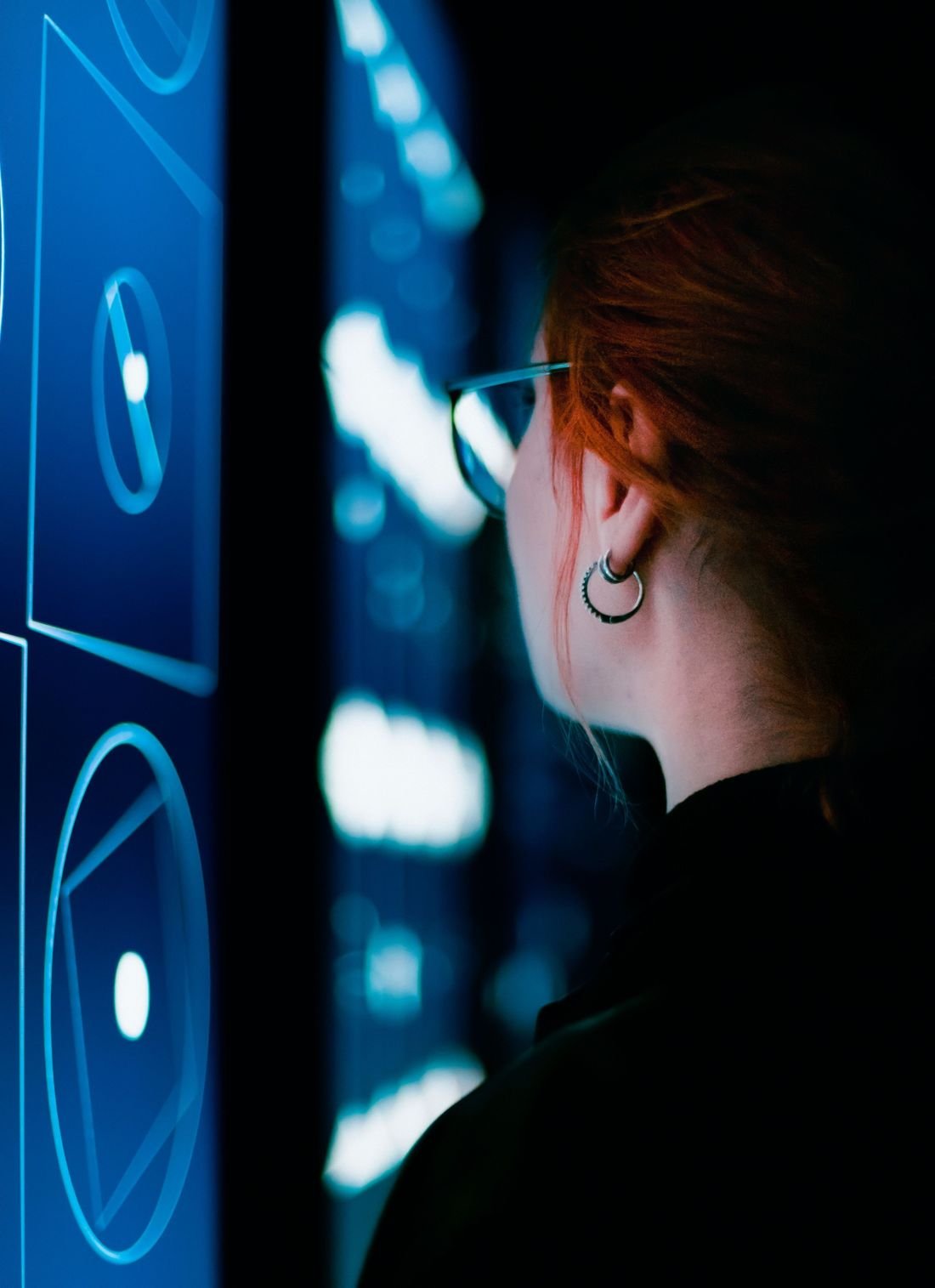 A woman with glasses studying glowing blue data screens